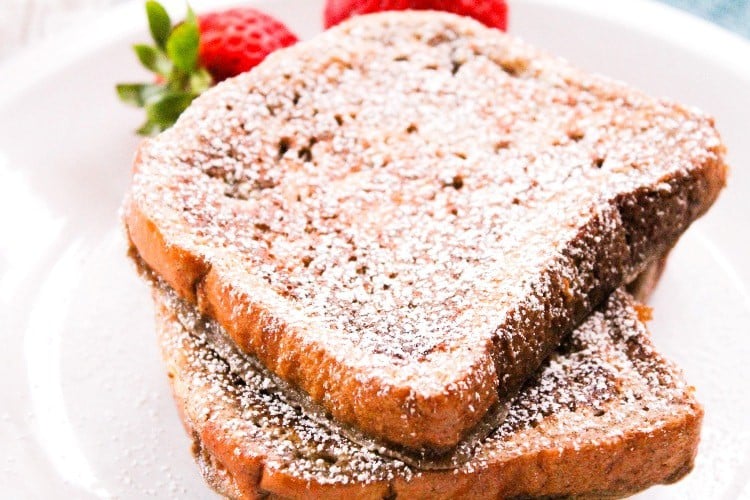 brioche french toast on a plate with powdered sugar and strawberries