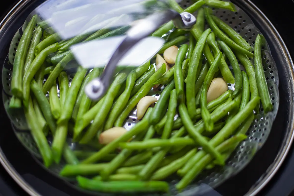 pot top over steaming green beans and garlic