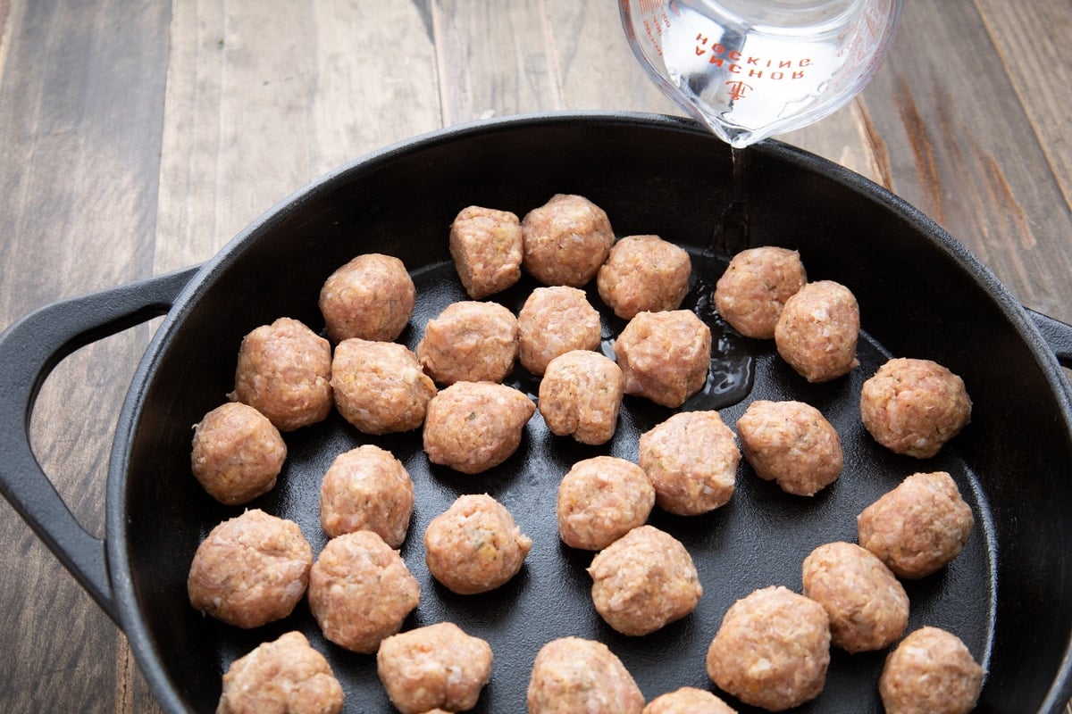 adding water to the pan to cook meatballs